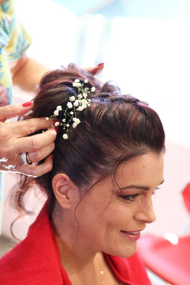 la coiffeuse ajuste une branche de gypsophile sur la coiffure de la mariée