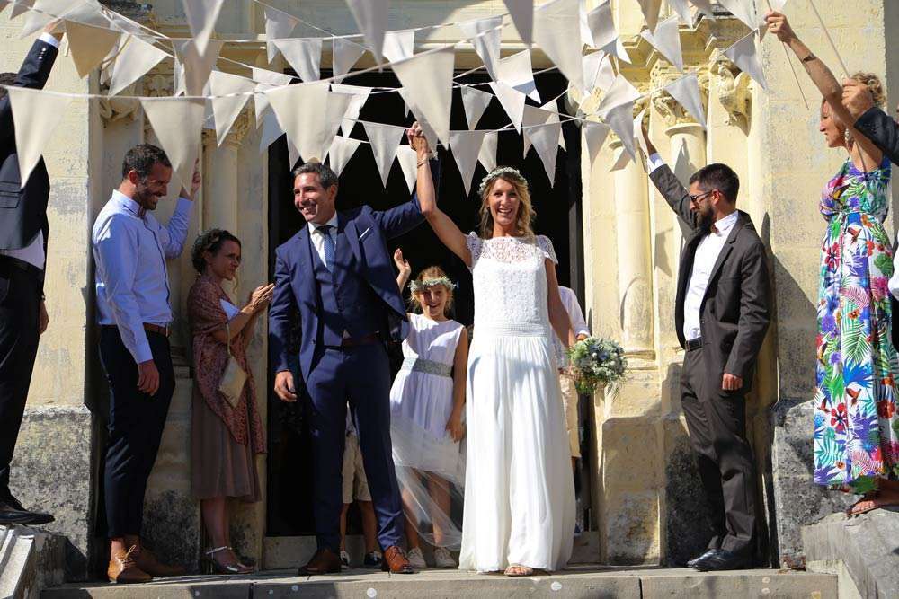 mariés ovationnés sur le perron de l'église qui se tiennent la main très haute