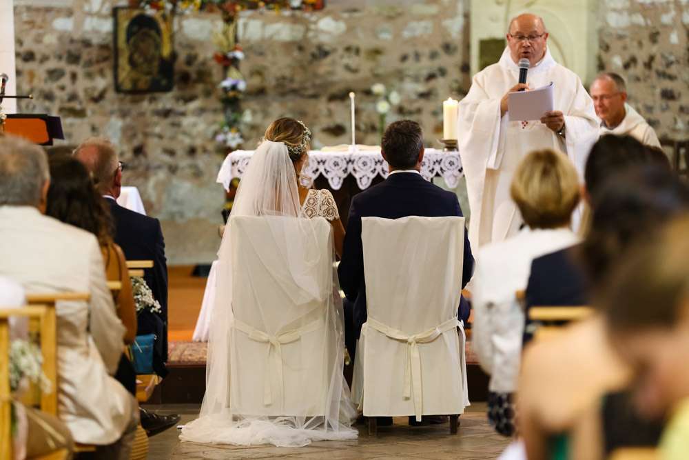 les mariés sont de dos à l'église qui regardent le prêtre