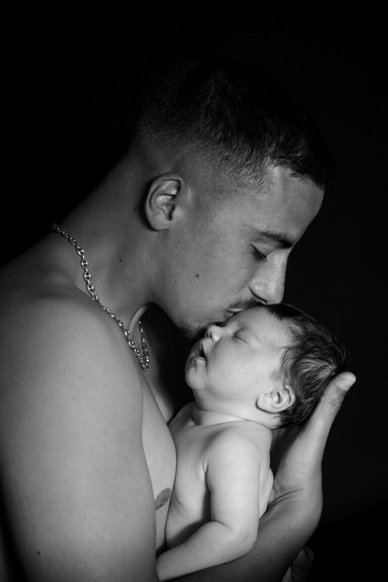 photo noir et blanc d'un jeune papa qui embrasse son nouveau-né sur le front